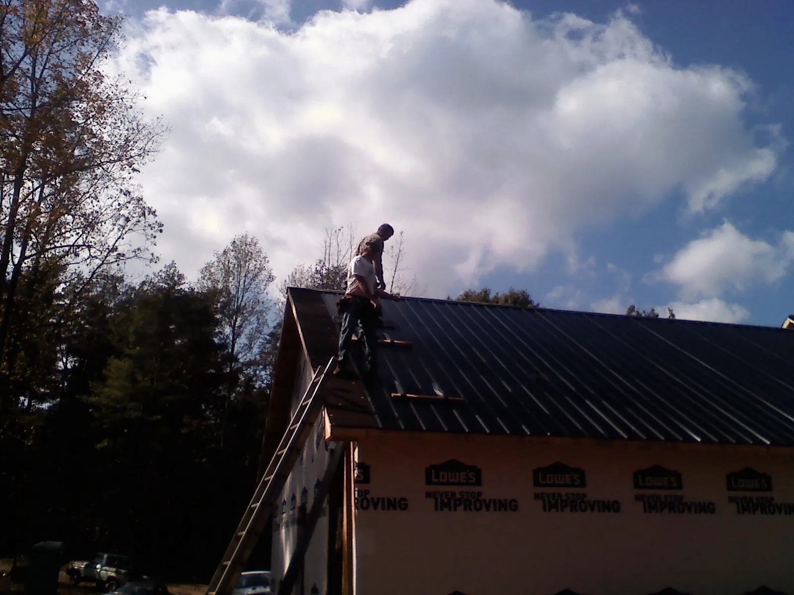 Roofer fastening dark metal panels high against a cloudy sky, from a Roof Inspection job in Cottonwood